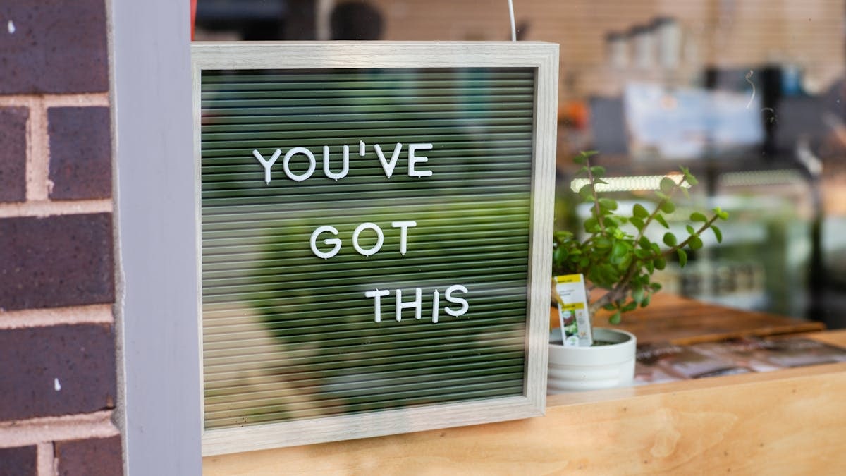 Vibrant image of a motivational sign 'YOU'VE GOT THIS' displayed in a cafe window next to a potted plant.
